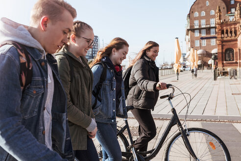 Seitenansicht von Freunden zu Fuß mit Teenager-Mädchen hält Fahrrad in der Stadt - MASF08836