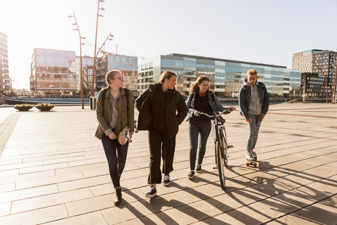 Teenager-Mädchen geht mit Fahrrad und Freunden spazieren, während ein Junge in der Stadt Fahrrad fährt, lizenzfreies Stockfoto