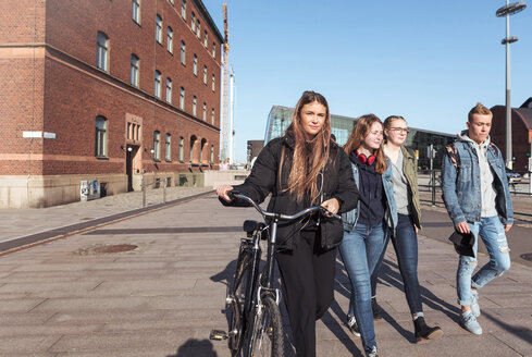 Teenager-Mädchen hält Fahrrad, während sie mit Freunden auf dem Fußweg in der Stadt gegen den klaren Himmel spazieren geht - MASF08839