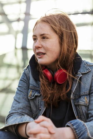 Teenager-Mädchen in Jeansjacke mit roten Kopfhörern schaut weg, lizenzfreies Stockfoto