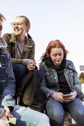 Teenager-Mädchen, das ein Mobiltelefon benutzt, während es mit Freunden vor einem klaren Himmel sitzt - MASF08841