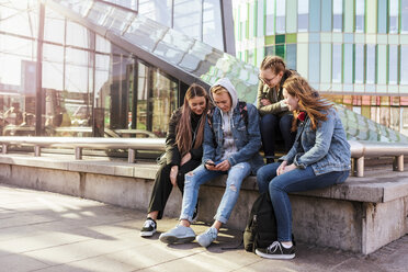 Teenage girls looking at friend using mobile phone while sitting by railing in city - MASF08846