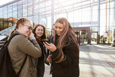 Teenager-Mädchen hören Musik über ihr Mobiltelefon, während sie mit Freunden vor dem Bahnhof stehen - MASF08849