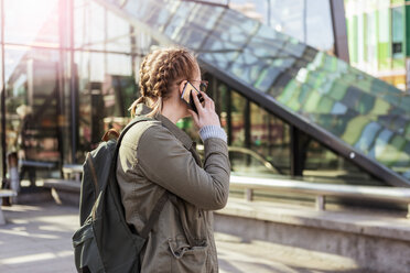 Teenage girl with backpack talking on mobile phone while standing in city - MASF08853