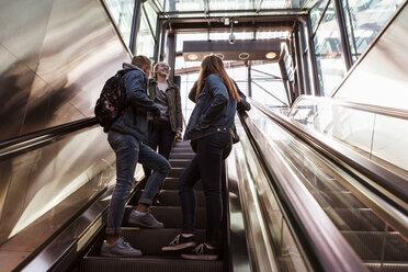 Low angle view of teenage friends talking while standing on escalator - MASF08854