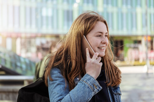 Lächelndes Teenager-Mädchen, das in der Stadt mit dem Handy telefoniert und wegschaut - MASF08855