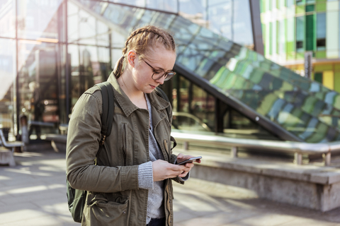 Teenager-Mädchen, das ein Mobiltelefon benutzt, während es an einem Gebäude in der Stadt steht, lizenzfreies Stockfoto