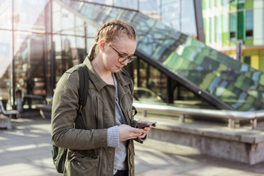 Teenager-Mädchen, das ein Mobiltelefon benutzt, während es an einem Gebäude in der Stadt steht - MASF08856