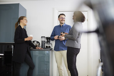 Lächelnde Geschäftskollegen, die sich bei einem Kaffee im Büro unterhalten - MASF08863