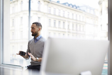 Geschäftsmann hält Tasse und gestikuliert gegen das Fenster im Büro - MASF08866