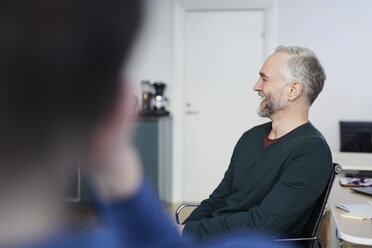 Smiling mature businessman sitting with colleague at office - MASF08870