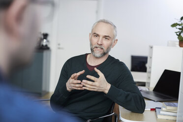 Reifer Geschäftsmann gestikuliert bei der Diskussion mit einem Mitarbeiter am Schreibtisch im Büro - MASF08871