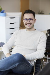 Porträt eines lächelnden Geschäftsmannes, der auf einem Stuhl im Büro sitzt - MASF08876