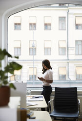 Seitenansicht einer reifen Geschäftsfrau, die ein Mobiltelefon benutzt, während sie am Fenster im Büro steht - MASF08883