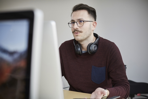 Geschäftsmann trägt Kopfhörer, während er einen Laptop am Schreibtisch im Büro benutzt, lizenzfreies Stockfoto