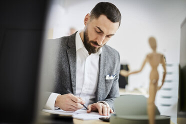 Mid adult businessman writing in note pad at desk in office - MASF08904