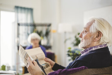 Älterer Mann liest Zeitung, während er auf dem Sofa im Pflegeheim sitzt - MASF08910