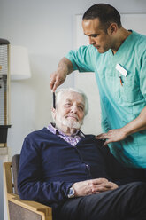 Älterer männlicher Pfleger kämmt die Haare eines älteren Mannes, der auf einem Stuhl im Pflegeheim sitzt - MASF08911