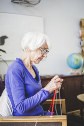 Ältere Frau strickt, während sie auf einem Stuhl im Pflegeheim sitzt - MASF08912