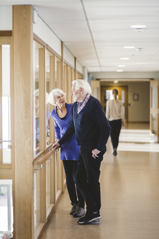 Älteres Ehepaar unterhält sich am Fenster im Korridor eines Pflegeheims, lizenzfreies Stockfoto