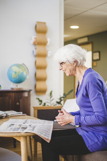 Seitenansicht einer lächelnden Seniorin beim Zeitungslesen am Tisch im Pflegeheim - MASF08916
