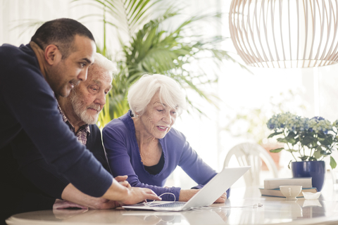 Älterer Mann benutzt Laptop mit Eltern am Tisch im Pflegeheim, lizenzfreies Stockfoto
