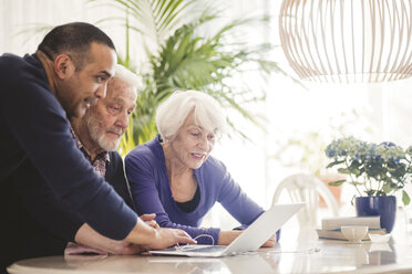 Mature man using laptop with parents at table in nursing home - MASF08918