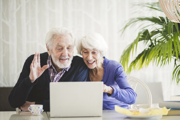 Cheerful senior couple video calling through laptop at table in nursing home - MASF08922