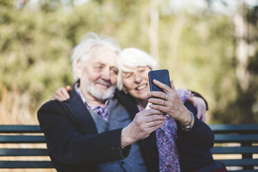 Smiling senior couple taking selfie while sitting on bench - MASF08934