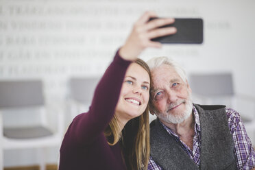 Smiling young woman taking selfie with grandfather while sitting in nursing home - MASF08944
