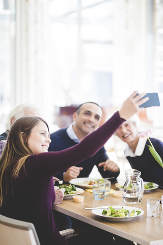 Junge Frau macht Selfie mit Vater und Großeltern beim Mittagessen im Pflegeheim, lizenzfreies Stockfoto