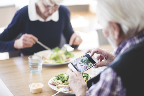Älterer Mann fotografiert Essen mit seinem Smartphone, während er mit einer Frau am Tisch zu Mittag isst, lizenzfreies Stockfoto