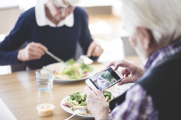 Senior man photographing food using smart phone while having lunch with woman at table - MASF08953