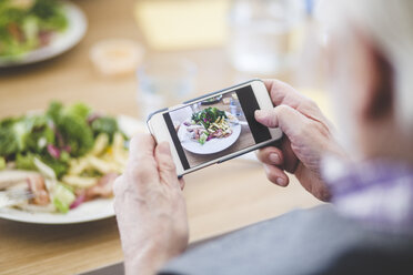 Ausgeschnittenes Bild eines älteren Mannes, der mit seinem Mobiltelefon am Tisch Essen fotografiert - MASF08954