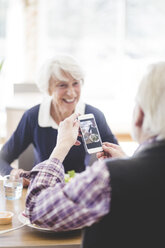 Senior man holding mobile phone while sitting with cheerful woman at table in nursing home - MASF08956