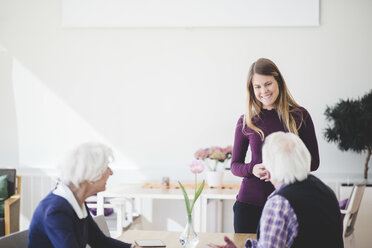 Enkelin lächelt im Gespräch mit den Großeltern, die in einem Pflegeheim am Tisch sitzen - MASF08959
