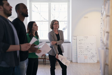 Multiethnische Ingenieure und Ingenieurinnen halten Dokumente und lesen Notizen an der Wand im Büro - MASF08968