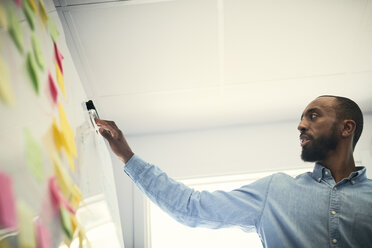 Niedriger Blickwinkel eines männlichen Ingenieurs, der Klebezettel auf einem Whiteboard im Büro liest - MASF08995