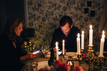 Männliche und weibliche reife Freunde benutzen ein Smartphone am Esstisch bei einer Dinnerparty - MASF09022