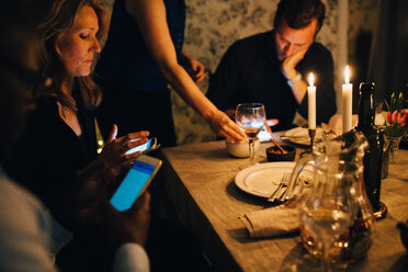 Ältere Freunde benutzen Mobiltelefone, während sie bei einem Abendessen am Tisch sitzen - MASF09025