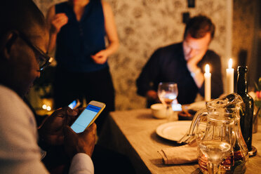 Reifer Mann, der sein Handy benutzt, während er mit Freunden auf einer Party zu Abend isst - MASF09027