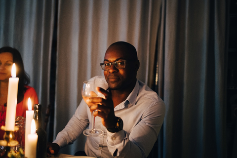 Porträt eines reifen Mannes, der mit einem Freund auf einer Dinnerparty sitzt und etwas trinkt, lizenzfreies Stockfoto