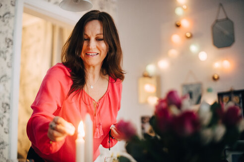Glückliche reife Frau beim Anzünden einer Kerze auf einer Party zu Hause - MASF09068