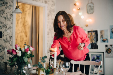 Smiling mature woman igniting candle at dining table in party - MASF09070