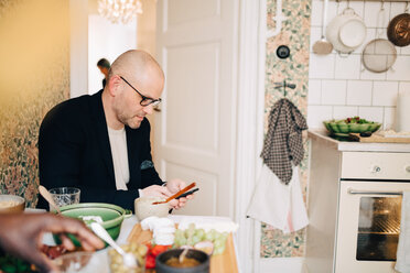 Mature man using mobile phone while sitting at dining table during party - MASF09095