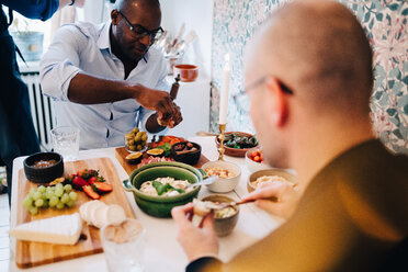 Mature friends with shaved head having food while sitting at table - MASF09104