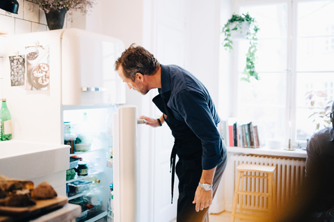 Älterer Mann schaut in den Kühlschrank, während er in der Küche steht, lizenzfreies Stockfoto