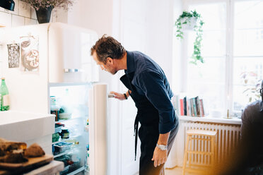 Mature man looking into refrigerator while standing at kitchen - MASF09105