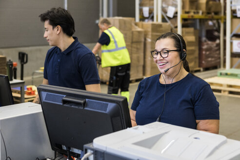 Lächelnde reife weibliche Kundendienstmitarbeiterin, die über ein Headset spricht, während sie neben einem Mitarbeiter im Vertrieb steht - MASF09110