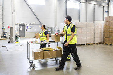 Multi-ethnic coworkers walking while pushing cart at distribution warehouse - MASF09142